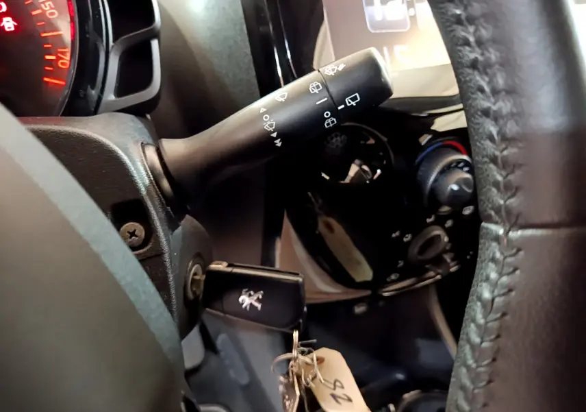 Gros plan sur le volant cuir et la clé Peugeot insérée, avec commandes d'essuie-glace et tableau de bord partiellement visibles.