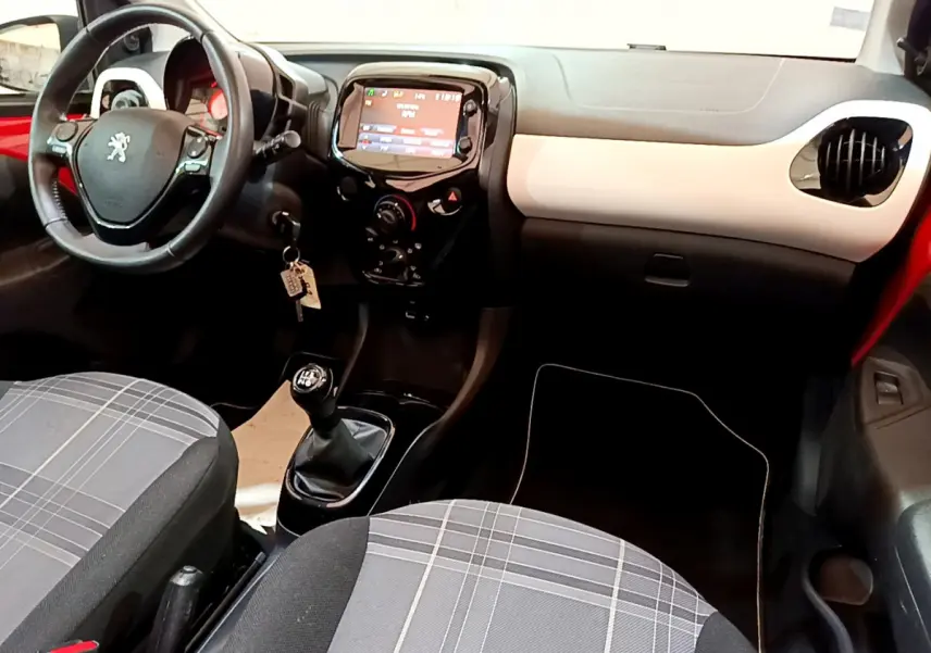 Intérieur avant de la Peugeot 108 rouge, vue côté conducteur, avec volant cuir et tableau de bord moderne.