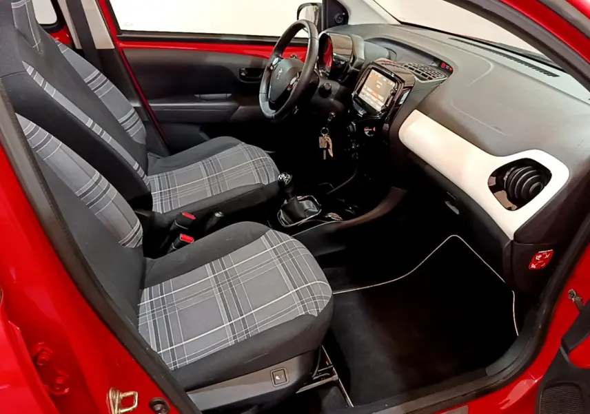 Vue intérieure côté conducteur du Peugeot 108 rouge 2017, sièges avant à motif à carreaux et tableau de bord noir et blanc.