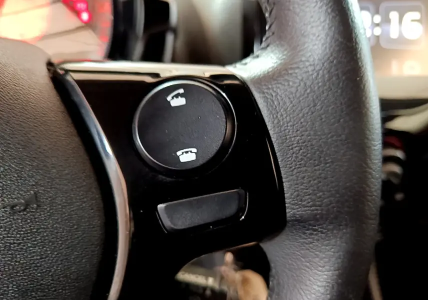 Gros plan sur les commandes téléphoniques du volant cuir du Peugeot 108 rouge, version 2017 essence.