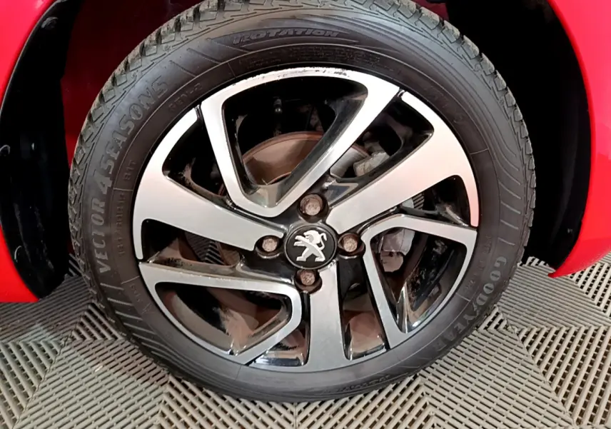 Gros plan sur la roue avant droite d'une Peugeot 108 rouge, mettant en valeur la jante alliage au logo lion central.