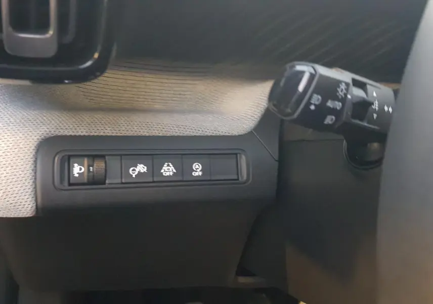 Gros plan sur les commandes d'assistance et réglage des phares à gauche du volant dans une Citroën C3 noire 2025.