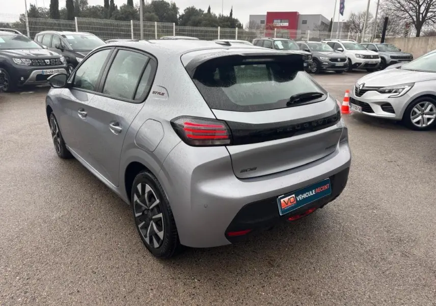 Vue 3/4 arrière gauche d'une Peugeot 208 Hybrid gris métallisé avec jantes 16 pouces et badge Style sous la pluie.