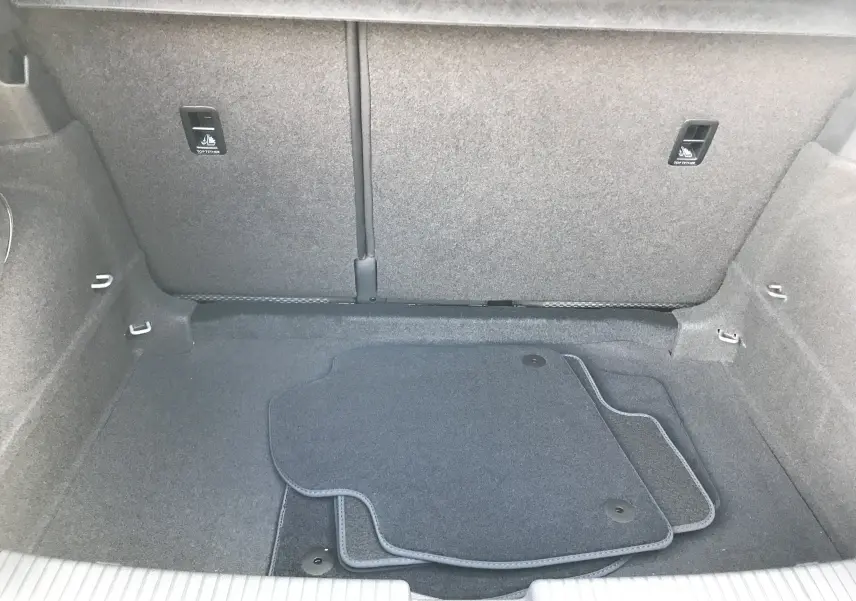 Coffre spacieux du Volkswagen T-Cross gris Limestone, vue intérieure arrière avec tapis de sol noirs posés.
