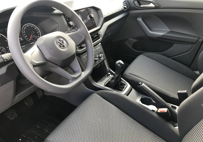 Intérieur avant droit du Volkswagen T-Cross 2020 gris Limestone, volant multifonction, sièges tissu noir et boîte manuelle.