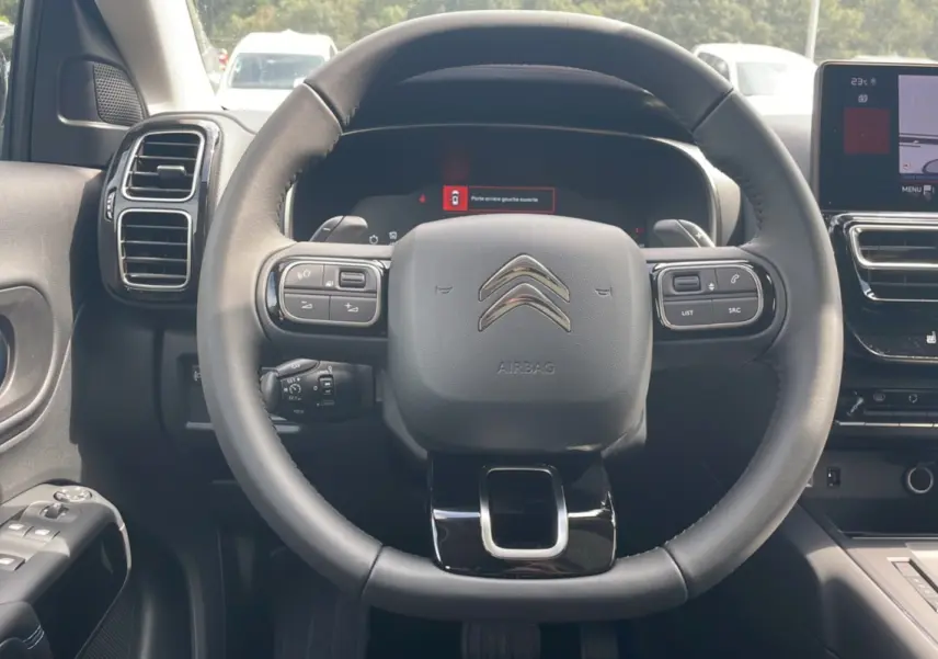 Vue intérieure centrée sur le volant du Citroën C5 Aircross Hybrid 2025, avec tableau de bord numérique et commandes au volant.