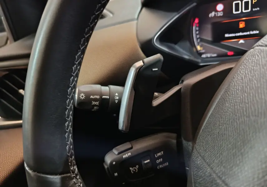 Gros plan sur le volant cuir et les commandes de régulateur de vitesse du DS3 Crossback gris foncé, tableau de bord numérique visible.