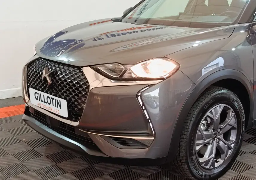 Vue 3/4 avant droit du DS3 Crossback gris foncé avec phares allumés et calandre distinctive en losange noir.