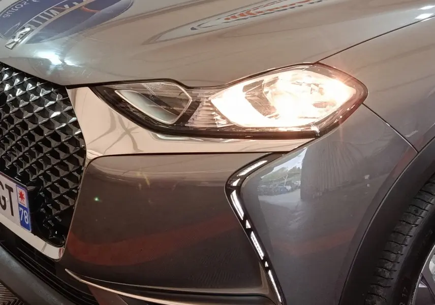 Gros plan sur l'avant droit gris foncé du DS3 Crossback avec phare allumé et calandre distinctive noire.