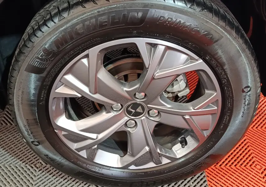 Gros plan sur la roue galette Michelin montée sur un DS3 Crossback gris foncé, vue latérale avec sol en caoutchouc rouge et gris.