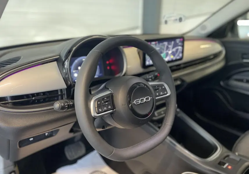 Vue intérieure du volant et tableau de bord beige métallisé du Fiat 600 1.2 Hybrid avec écran tactile central.