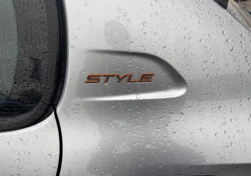 Gros plan sur l’inscription « Style » orange sur la portière grise mouillée d’une Peugeot 208 Hybrid 100 e-DCS6.
