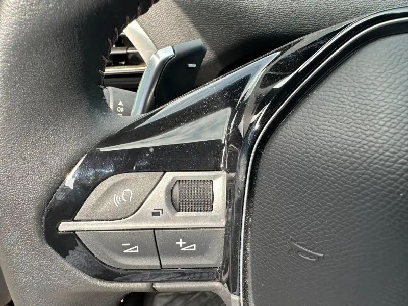 Gros plan sur les commandes gauche du volant cuir noir du Peugeot 3008 bleu hybride rechargeable 2024.