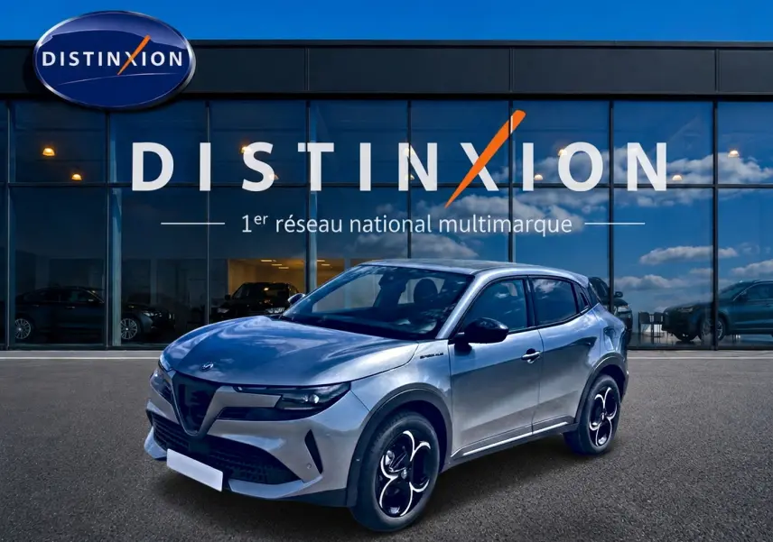 Vue 3/4 avant d'un Alfa Romeo Junior gris avec jantes alliage noires et toit noir devant une vitrine Distinxion.