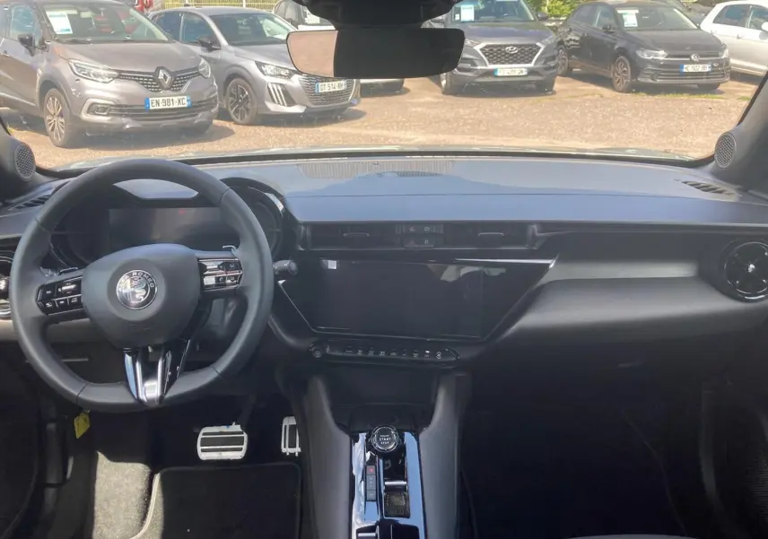 Vue intérieure avant de l'Alfa Romeo Junior 1.2 hybride grise, tableau de bord épuré avec écran tactile et volant multifonction.