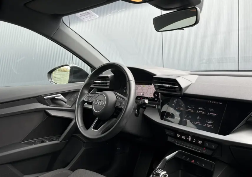 Intérieur Audi A3 Berline gris, vue côté conducteur, volant cuir multifonctions et écran tactile MMI visible.