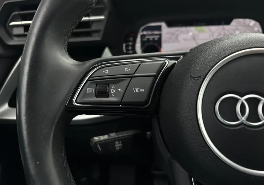 Gros plan sur le volant cuir noir multifonctions de l'Audi A3 Berline 35 TFSI 2020 avec affichage numérique en arrière-plan.