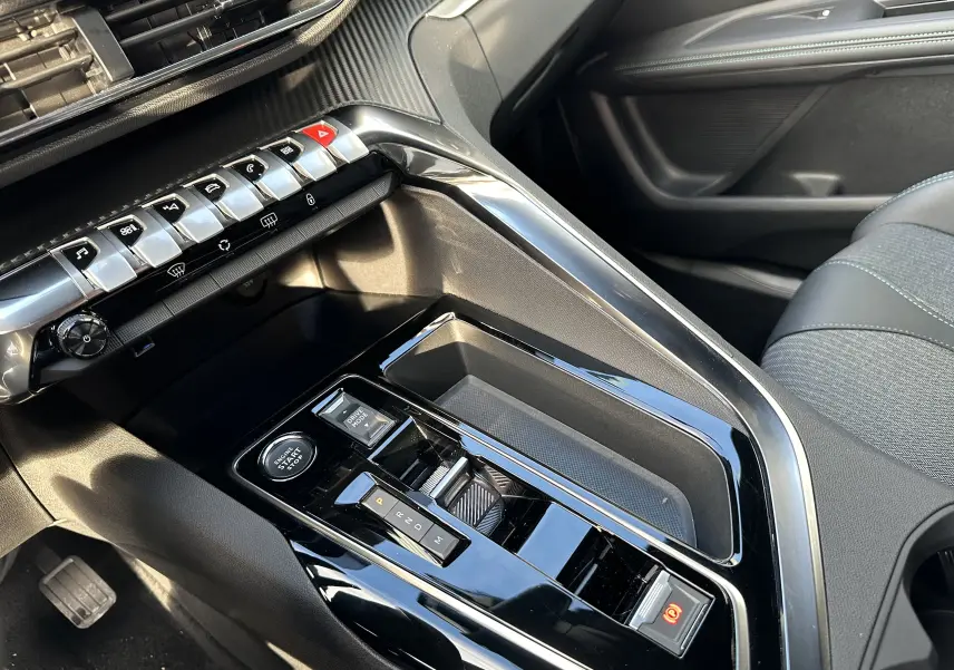 Vue rapprochée de la console centrale noire brillante du Peugeot 3008 blanc nacré 2024 avec commandes de boîte auto et boutons métallisés.