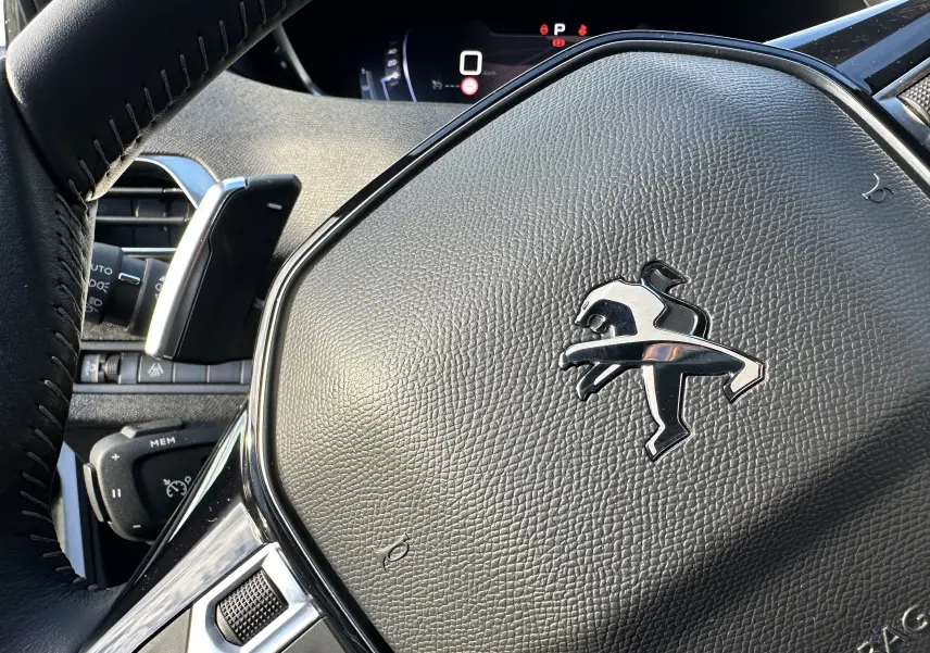 Gros plan sur le volant en cuir noir avec logo Peugeot du SUV 3008 2024, version diesel blanc nacré.