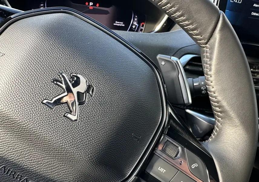 Gros plan sur le volant en cuir noir du Peugeot 3008 2024, avec logo lion et commandes intégrées visibles.