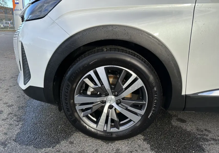 Gros plan sur la roue avant gauche d'un Peugeot 3008 blanc nacré, mettant en valeur la jante alliage et le pneu Michelin.