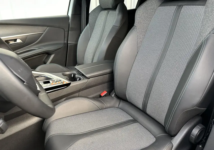 Gros plan sur les sièges avant en tissu et cuir noir du Peugeot 3008 2024, avec console centrale et accoudoir visibles.