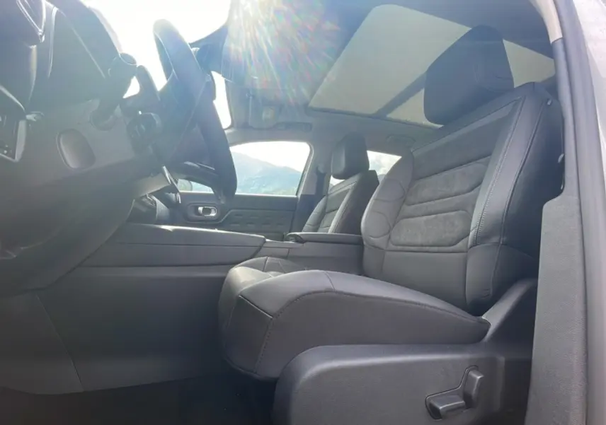Intérieur du Citroën C5 Aircross Hybrid 2025 vu côté conducteur, sièges noirs et toit panoramique lumineux.