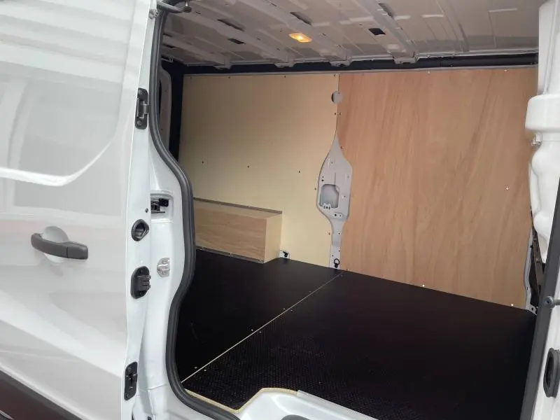 Vue intérieure arrière droite du Renault Trafic Fourgon blanc glacier, montrant l'espace de chargement avec cloison bois et plancher noir antidérapant.