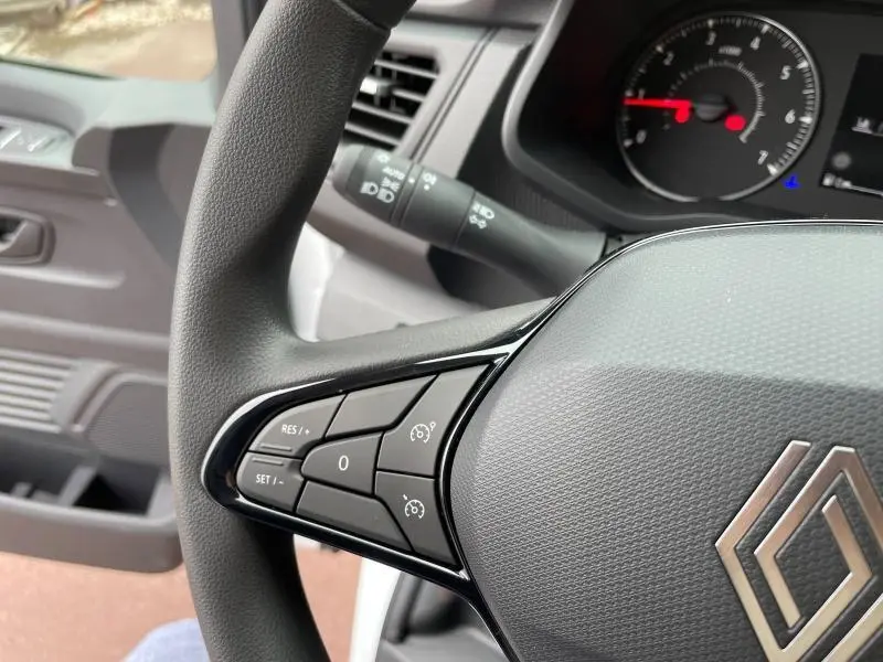 Gros plan sur le volant noir du Renault Trafic Fourgon blanc glacier, montrant les commandes de régulateur de vitesse côté gauche.