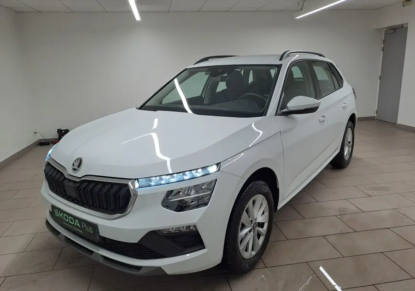 Vue 3/4 avant d'un Skoda Kamiq blanc Lune avec calandre noire et feux LED allumés dans un intérieur neutre.