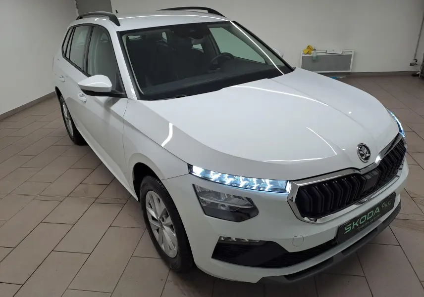 Vue 3/4 avant gauche du Skoda Kamiq blanc Lune avec feux LED allumés et calandre noire distinctive.