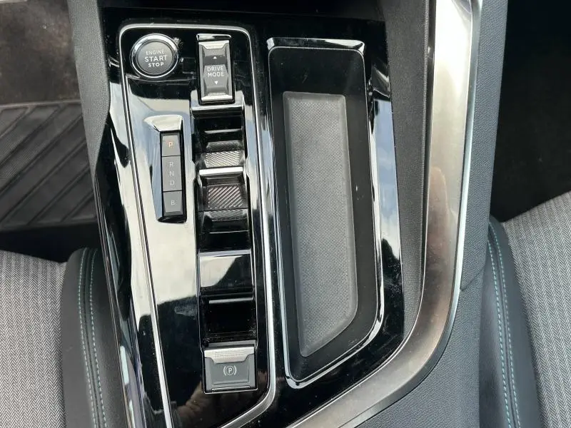 Gros plan sur la console centrale noire brillante du Peugeot 3008 hybride rechargeable 2024 avec boutons start/stop et sélecteur de mode.
