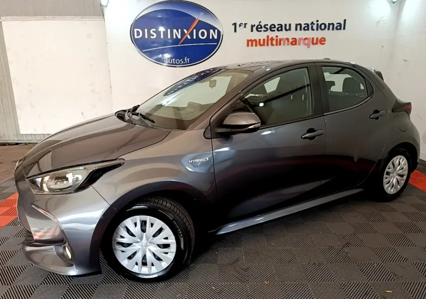 Toyota Yaris hybride gris clair vue de profil côté gauche, avec badge Hybrid et feux avant allumés.