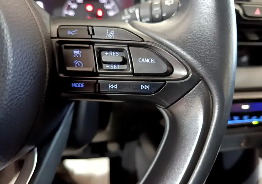 Gros plan sur les commandes du volant cuir de la Toyota Yaris hybride 2021, avec boutons de régulateur et assistance.