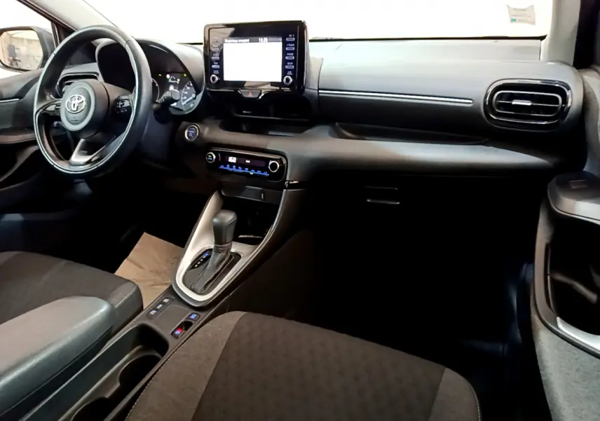 Intérieur avant de la Toyota Yaris Hybride 116h 2021, tableau de bord noir avec écran tactile central et volant cuir multifonctions.