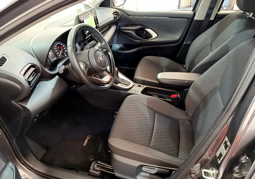 Intérieur avant droit d'une Toyota Yaris hybride gris clair, volant cuir, sièges tissu gris et écran tactile central.