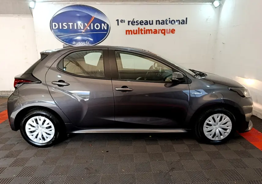 Profil droit d'une Toyota Yaris hybride gris clair 2021 avec jantes argentées et badge Hybrid sur l'aile avant.