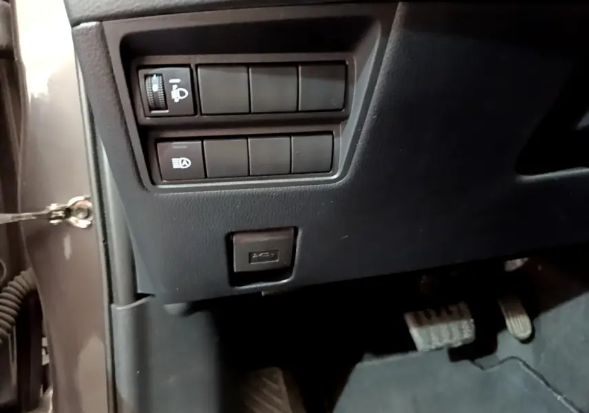 Vue rapprochée des commandes d'éclairage et port USB sous le tableau de bord côté gauche d'une Toyota Yaris gris clair.