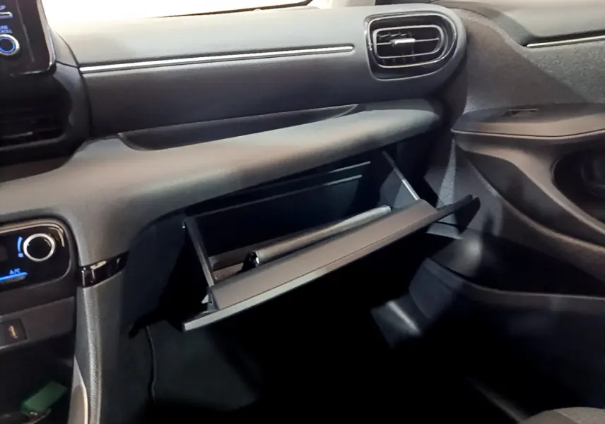 Intérieur de la Toyota Yaris hybride 2021, vue côté passager sur la boîte à gants ouverte et tableau de bord gris foncé.