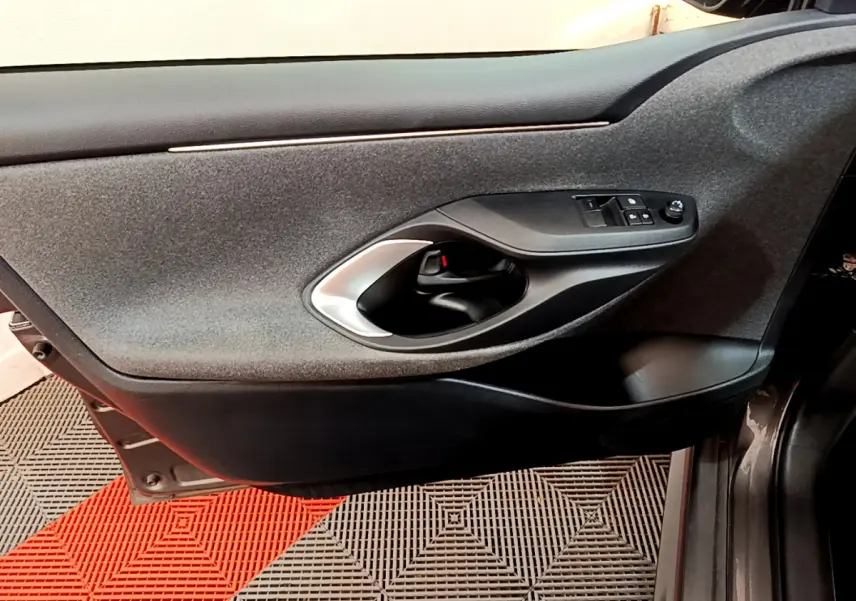 Vue côté gauche de la porte intérieure grise de la Toyota Yaris hybride 2021 avec commandes de vitres et poignée argentée.