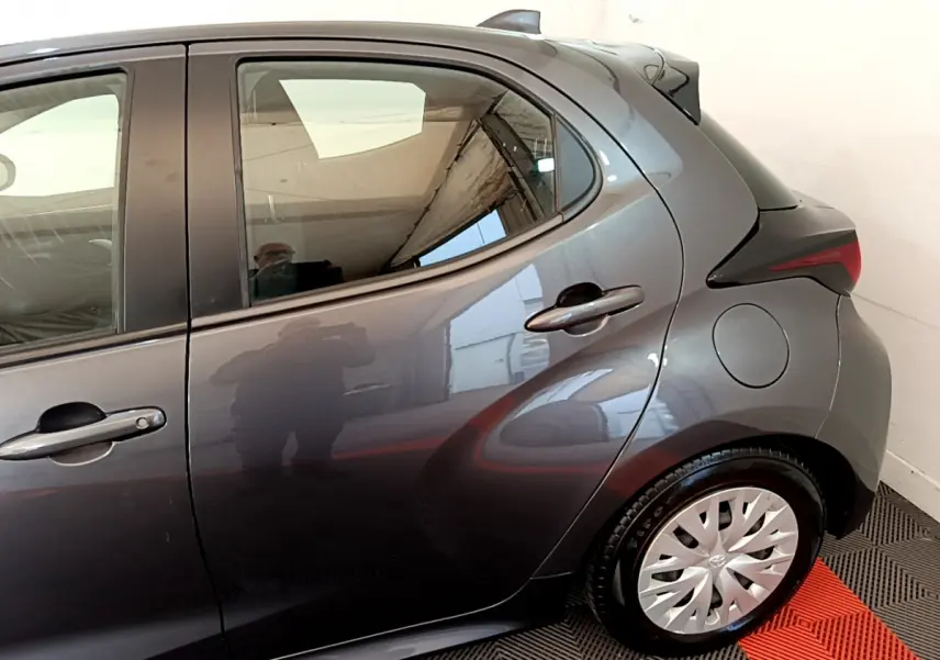 Vue côté droit arrière d'une Toyota Yaris hybride gris clair, mettant en valeur la porte arrière et la roue avec enjoliveur.