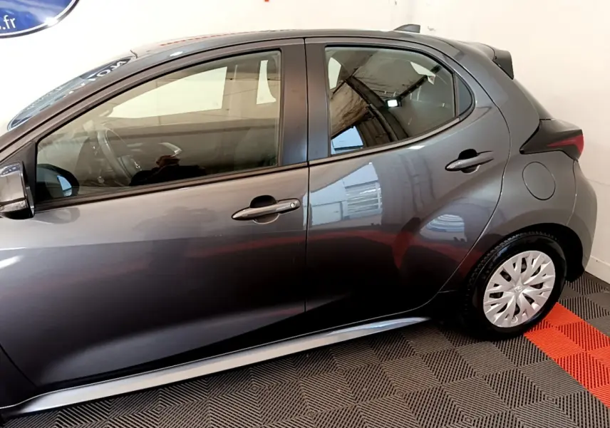Profil côté gauche de la Toyota Yaris hybride gris clair 2021, avec jantes acier et poignées de porte assorties.