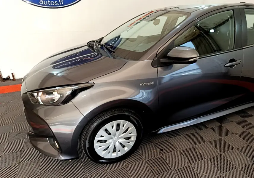 Vue 3/4 avant gauche d'une Toyota Yaris hybride gris clair avec jante acier et logo Hybrid sur l'aile avant.