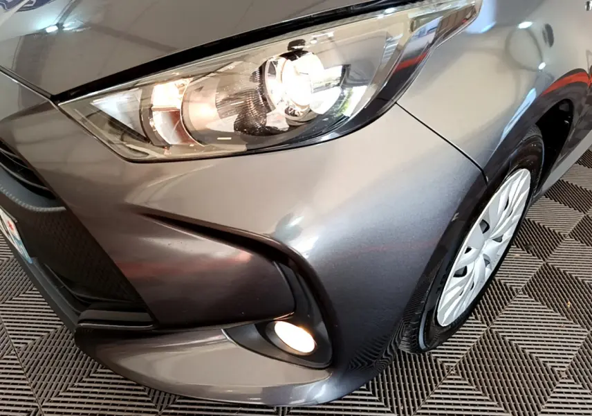 Gros plan sur l'avant droit gris clair d'une Toyota Yaris hybride 2021 avec phares et antibrouillards allumés.