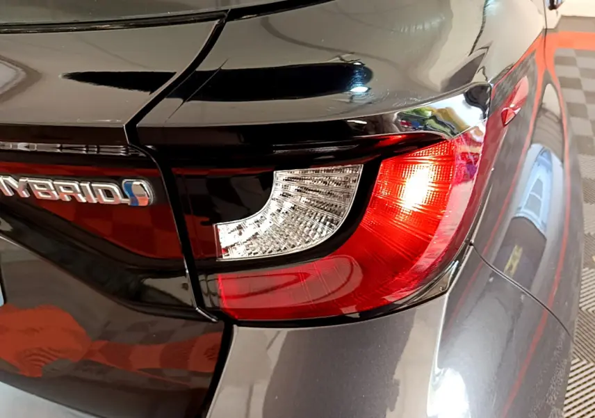 Gros plan sur le feu arrière droit rouge et blanc d'une Toyota Yaris hybride gris clair avec logo Hybrid visible.