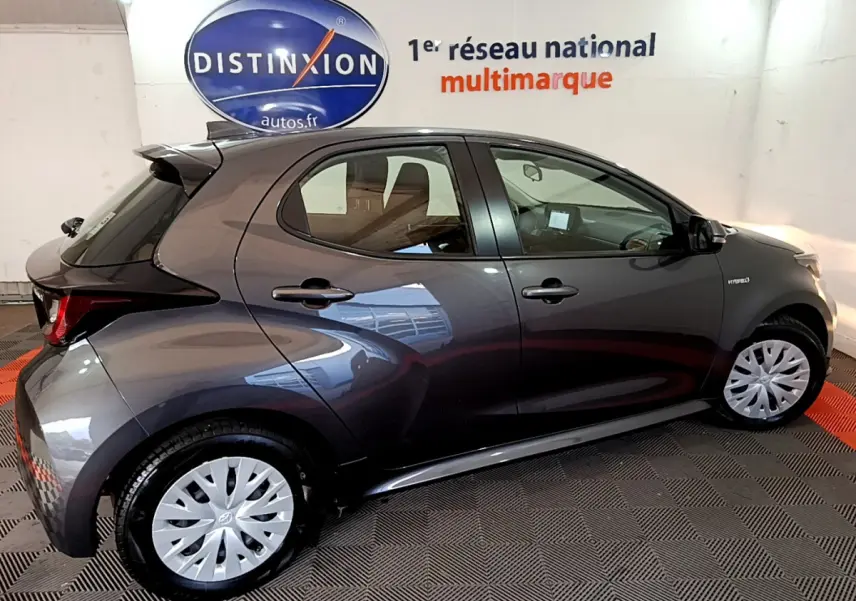 Profil côté gauche d'une Toyota Yaris hybride gris clair 2021 avec jantes et logo hybride visible sur l'aile avant.