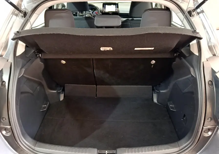 Coffre ouvert vu de l'arrière d'une Toyota Yaris hybride gris clair, banquette arrière et tableau de bord visibles.