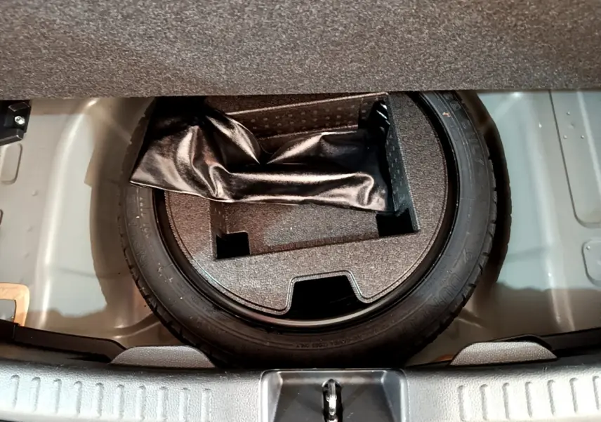 Vue plongeante sur la roue de secours et le rangement sous le plancher du coffre d'une Toyota Yaris gris clair hybride.