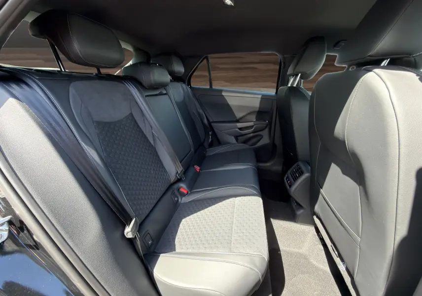 Vue intérieure arrière droite du Volkswagen T-Roc 2026 noir ébène, sièges en cuir et tissu avec ceintures de sécurité visibles.