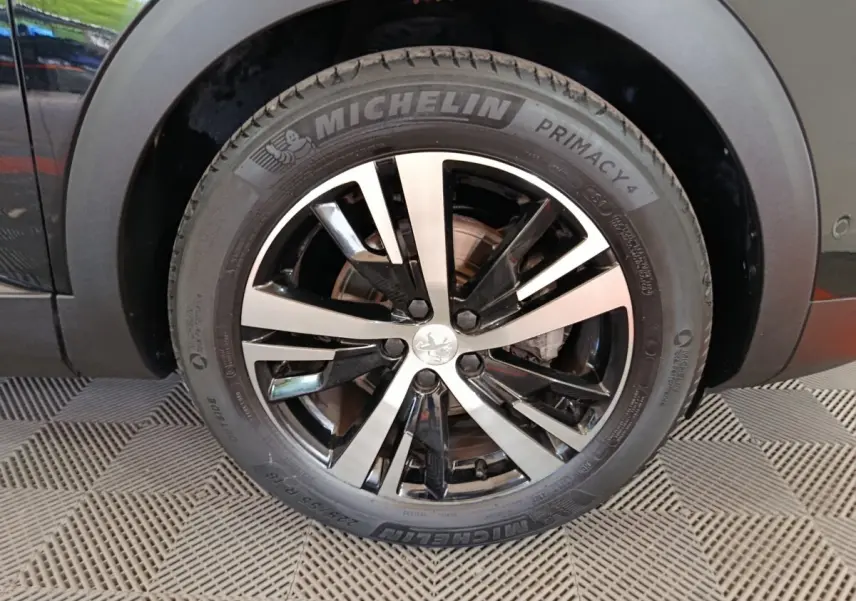 Gros plan sur la roue avant gauche noire du Peugeot 3008 PureTech 130 GT avec jante alliage bicolore et pneu Michelin.